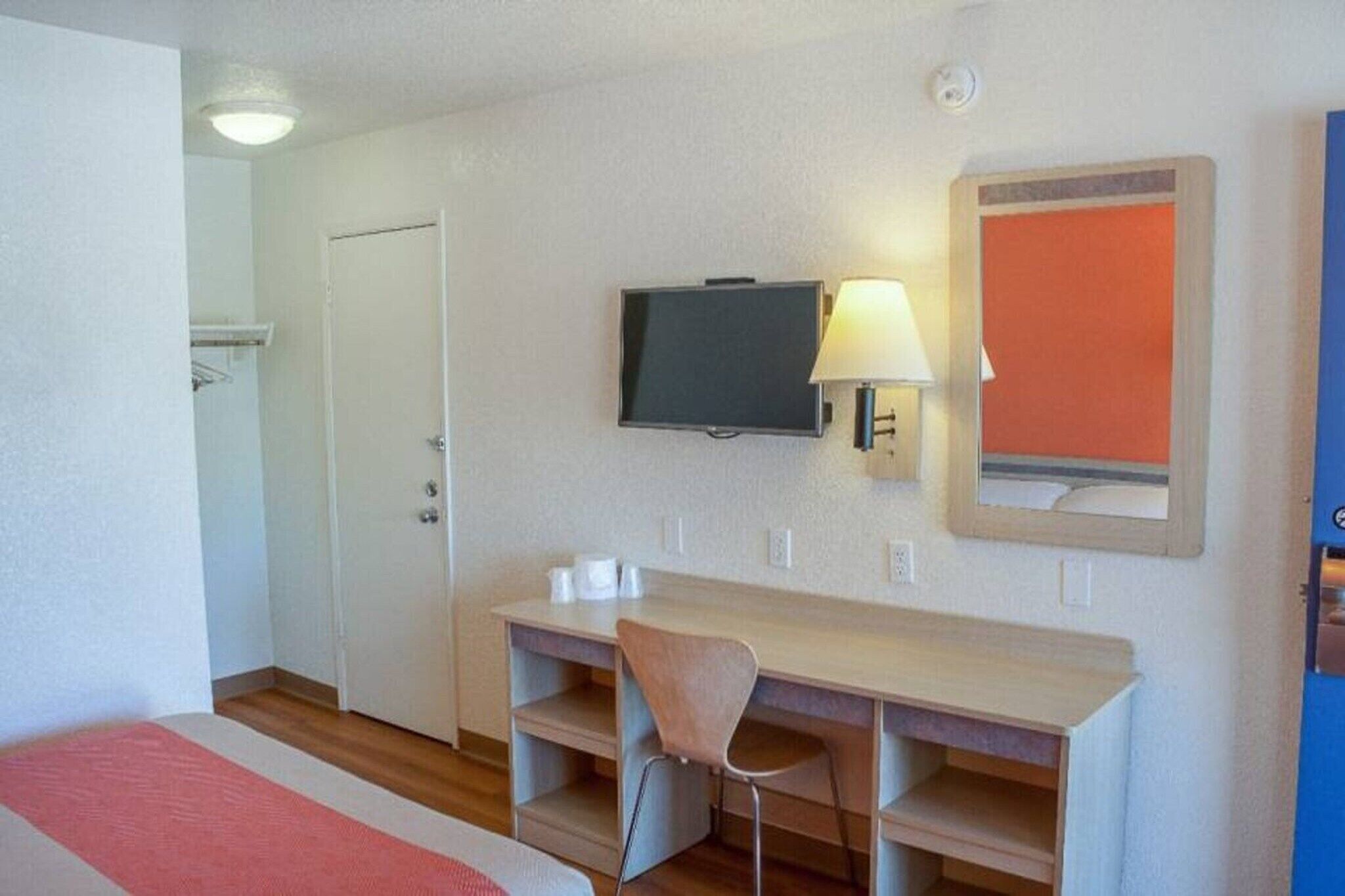 Ett hotellrum med ett skrivbord, en stol, en tv och en spegel.