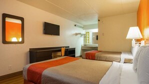 A hotel room with two beds, a TV, a desk, and a bathroom mirror.