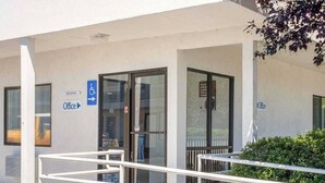 An office building with a wheelchair-accessible entrance, a sign indicating the office location, and a glass door.