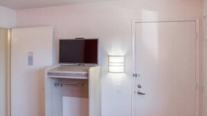 A room with a television mounted on a shelf, a door with a light above it, and a closed door to the right. - 2 Full Beds | Mini Fridge (Ukiah)