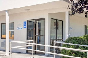 An office building with a wheelchair-accessible entrance, a sign indicating the office location, and a glass door.