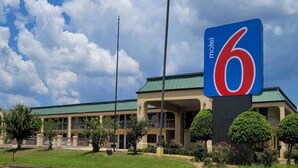 A motel with a large sign, a green roof, and a parking lot.