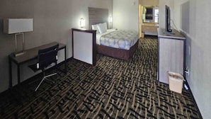 A hotel room with a bed, desk, chair, TV, and a trash bin.