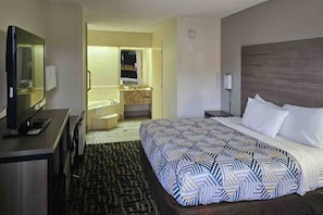 Una camera d'albergo con un letto, una televisione, una scrivania, un bagno con un lavandino e uno specchio, e un tappeto decorato.