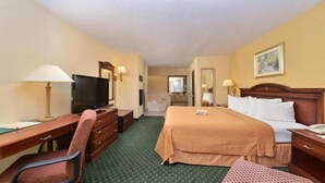 A hotel room with a bed, desk, chair, television, and a bathroom visible in the background.