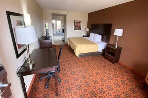 Una habitación de hotel con cama, escritorio, silla, lámparas y alfombra estampada.