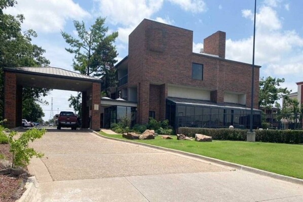 Un edificio moderno con entrada cubierta, fachada de ladrillo y césped bien cuidado.
