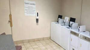 A guest laundry area with a sign, a wall-mounted soap dispenser, and a row of washing machines. - 2 Queen Beds | Smoking, Micfridge (Oklahoma City OK)