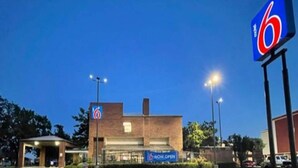 Un motel à six côtés, avec une enseigne indiquant « OUVERT MAINTENANT », un parking et un ciel dégagé.