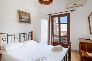 Ein Schlafzimmer mit Bett, einem Holztisch, einem Spiegel, einem Gemälde und einem Fenster mit Vorhängen.