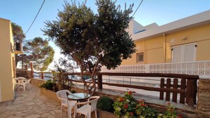 A stone patio with a table and chairs, a wooden fence, and a row of flowering plants. - Standard Double Room Apartment with Shared Garden and Wi-Fi (Mpatsi)
