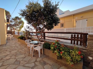 Une terrasse en pierre avec une table et des chaises, une clôture en bois et une rangée de plantes en fleurs.