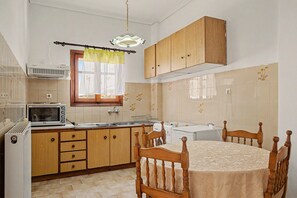 A compact kitchen with wooden cabinets, a microwave, a sink, and a dining table with chairs.