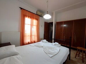 A hotel room with a bed, a wardrobe, a radiator, and a window with curtains.