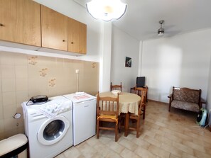 A compact kitchen with a washing machine, a dining table with chairs, and a ceiling fan.