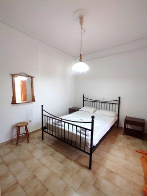 A bedroom with a bed, a nightstand, a wooden stool, a mirror, and a hanging light fixture.