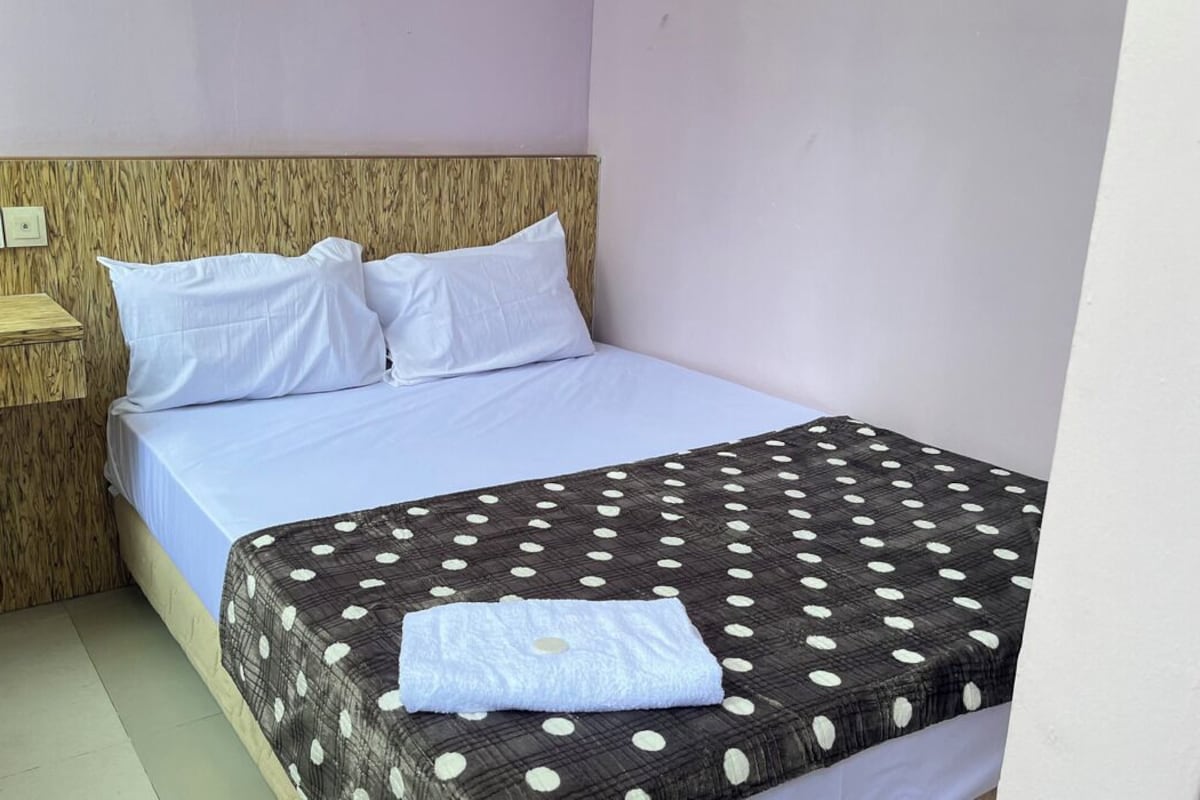 Una cama individual con una colcha de lunares, cabecera de madera y un cubo de basura azul.