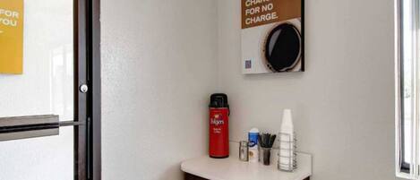 A hotel room with a coffee machine, a cup holder, and a sign stating 'YOUR MORNING CHARGE UP FOR NO CHARGE.'