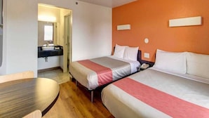 Une chambre d’hôtel avec deux lits, une table en bois, une salle de bain avec un lavabo et un mur d’accent de couleur orange.