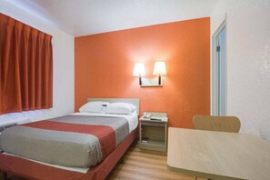 Une chambre d’hôtel comprenant un lit, une table de chevet, une lampe et une petite table avec une chaise.