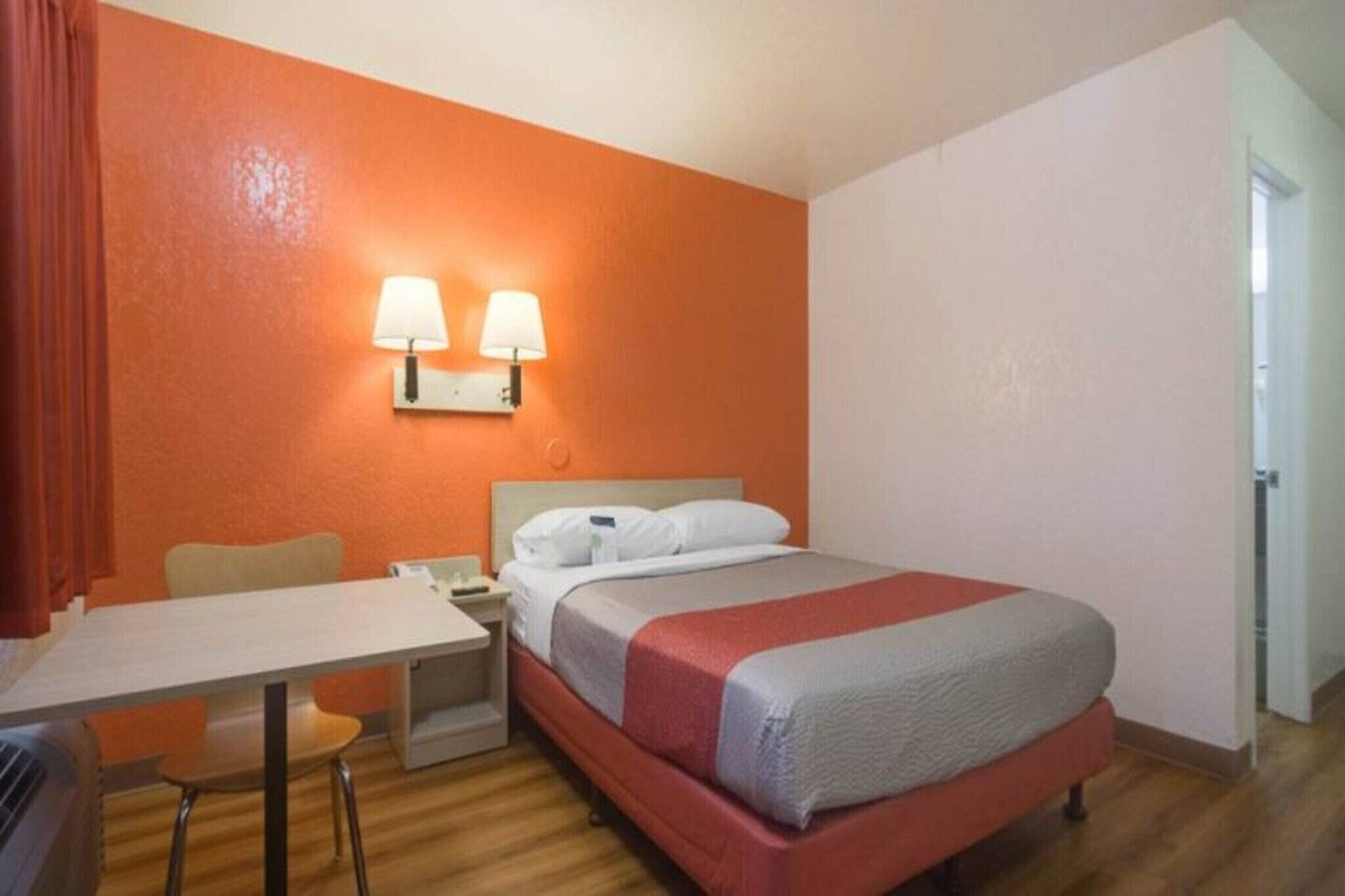 A hotel room with a bed, a desk, two bedside lamps, and a chair.