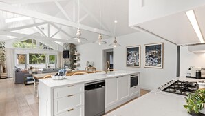 Uma cozinha moderna com armários brancos, uma ilha grande com lava-louças, luminárias pendentes e fogão a gás.
