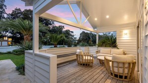 Uma área externa coberta com deck de madeira, assentos e vista para o verde ao redor.