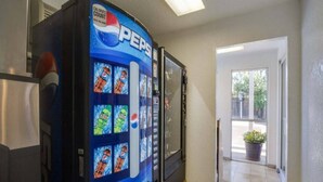 Una máquina expendedora con el logotipo de Pepsi, un refrigerador y una puerta que da a un área exterior con una planta en maceta.