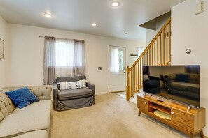 A living room with a sofa, a chair, a television, and a wooden staircase.