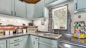 Een keuken met lichtblauwe kastjes, een granieten aanrechtblad, een roestvrijstalen spoelbak en een accentmuur van steen.
