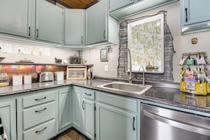 Une cuisine avec des meubles de couleur bleu clair, un comptoir en granit, un évier en acier inoxydable et un mur décoratif en pierre.