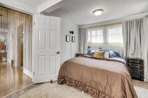 Ein Schlafzimmer mit einem großen Bett, einer Tür, einem Fenster mit Vorhängen und einem Schminktisch.