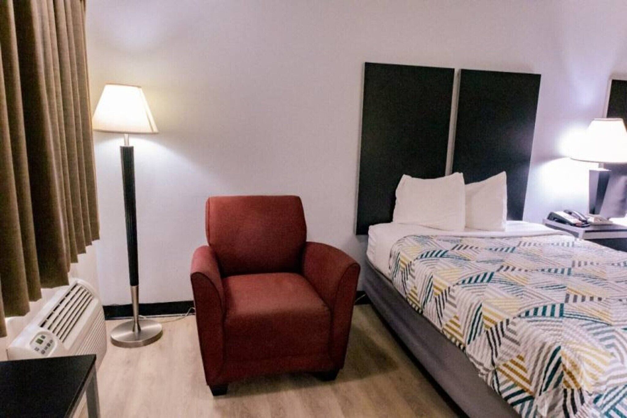 Ein Hotelzimmer mit einem Bett, einem roten Sessel, einer Stehlampe und einer Bodentaste.