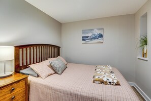 A bedroom with a bed, a nightstand, a lamp, a wall-mounted painting, and a potted plant.