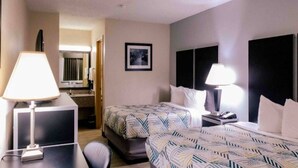 Une chambre d’hôtel avec deux lits, un bureau, une chaise, une lampe, un tableau au mur et une fenêtre.