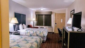 Une chambre d’hôtel avec deux lits, un bureau, une télévision et une fenêtre avec des rideaux.