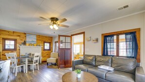 Ein Zimmer mit Holzboden, Ledersofa, Esstisch mit Stühlen, Deckenventilator und Kamin.