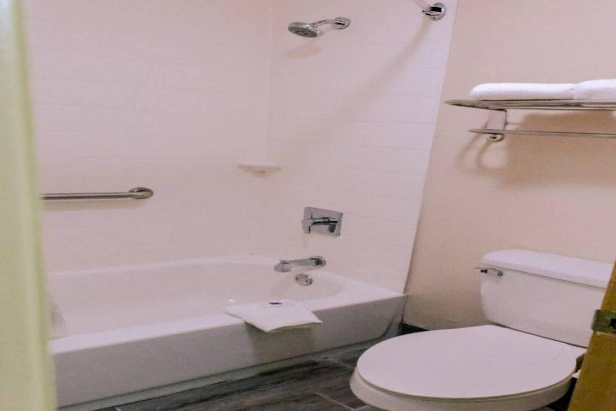A bathroom with a bathtub, toilet, and a shelf with towels.