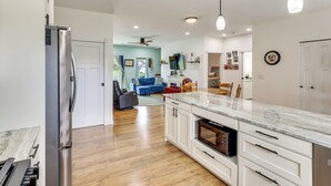 Una cocina moderna con refrigerador de acero inoxidable, armarios blancos, encimera de mármol y ventilador de techo.