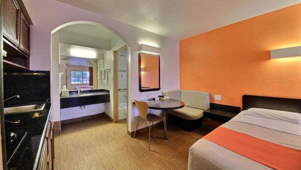 A hotel room with a bed, a small table, a chair, a mirror, and a kitchenette. - 1 King Bed | Smoking (Edinburg)