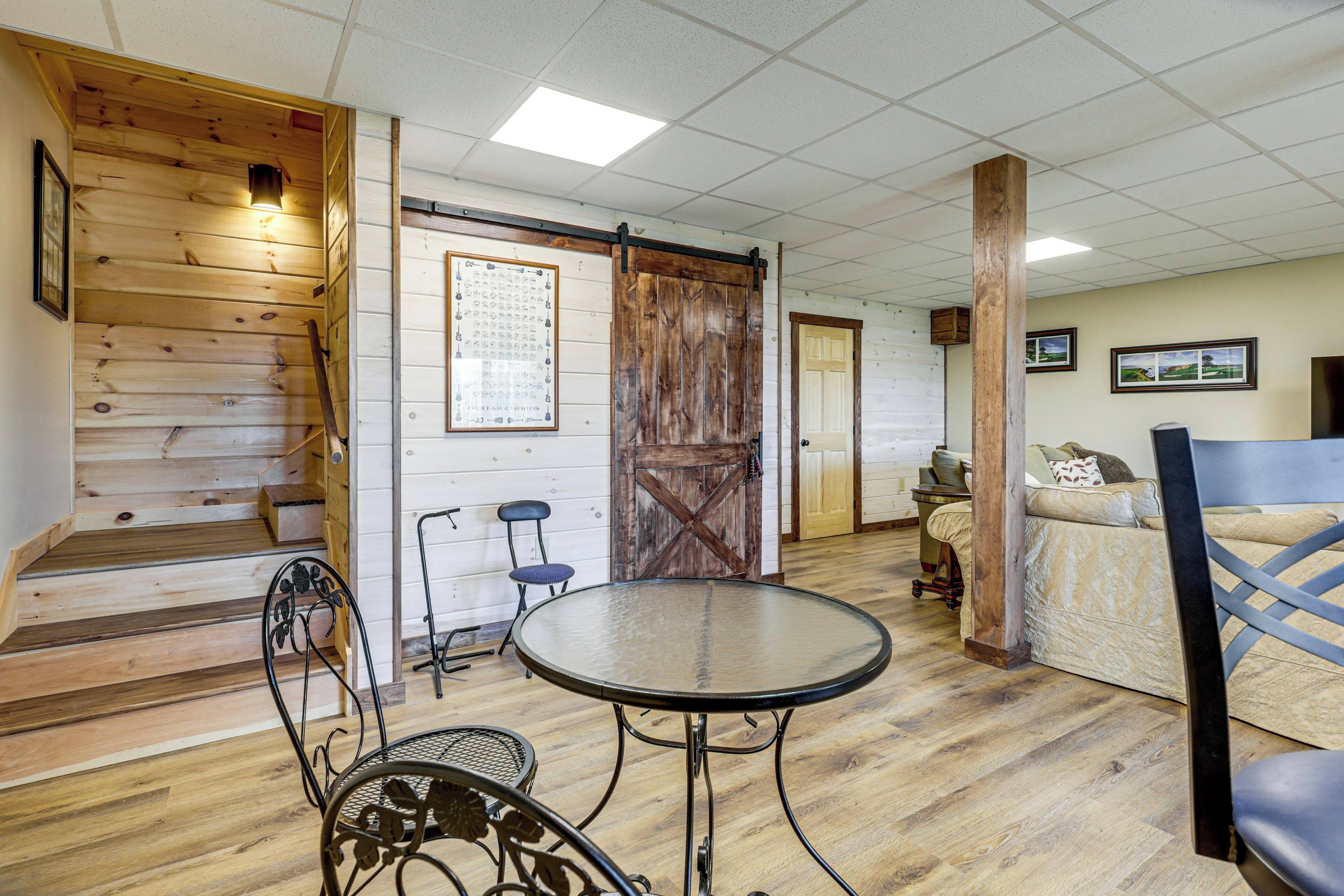 Una habitación con escalera de madera, una mesa redonda, sillas de metal, un sofá y una puerta de estilo de granero.