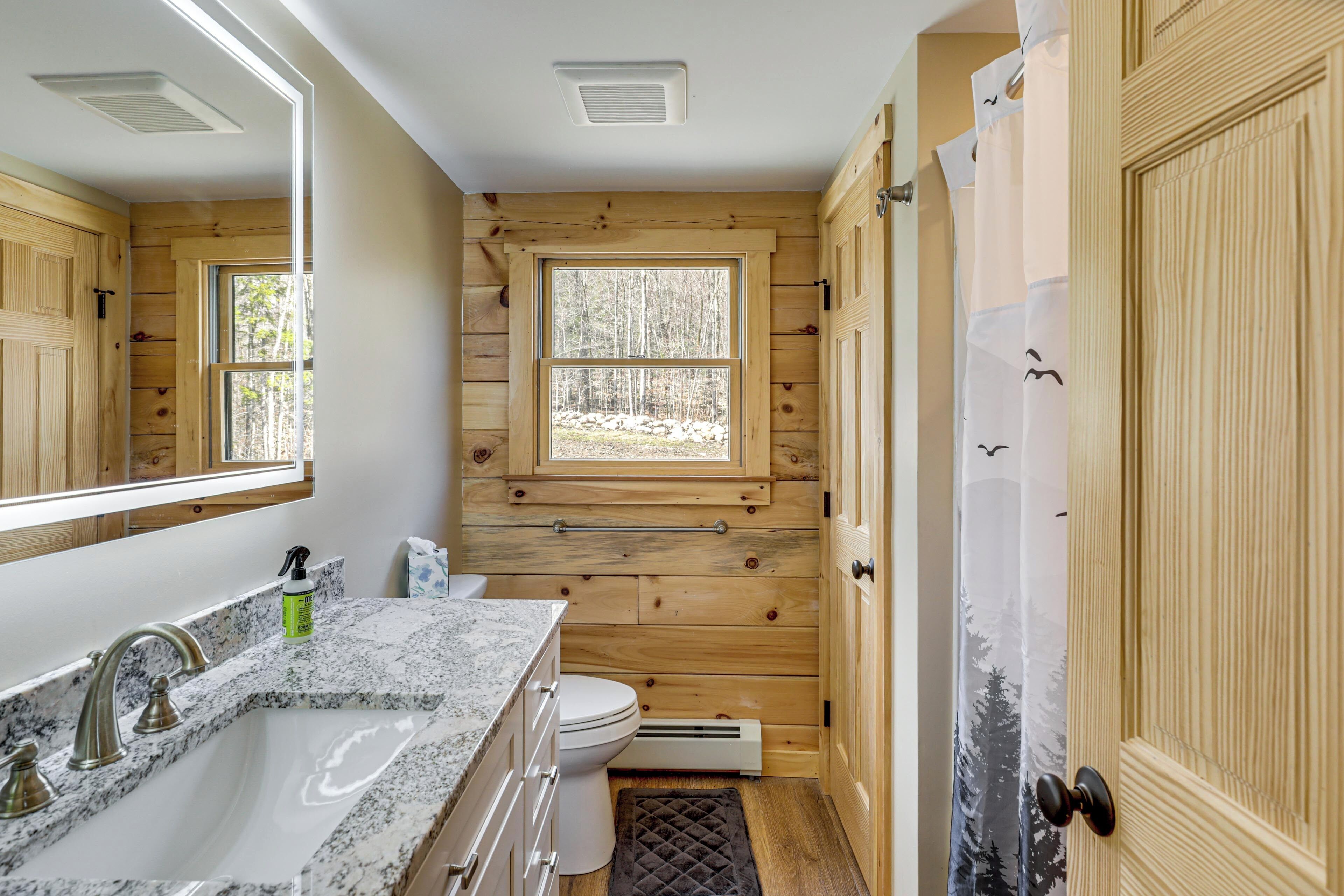 A bathroom with wooden walls, a window, a sink, and a toilet.