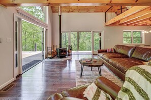 A spacious living room with a fireplace, leather sofa, and large windows. - 'The Appalachian Hideaway' w/ Hiking Trails & Deck (Spencer)