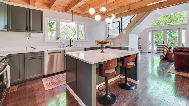 A modern kitchen with a central island, bar stools, and a dining area with a sofa. - 'The Appalachian Hideaway' w/ Hiking Trails & Deck (Spencer)