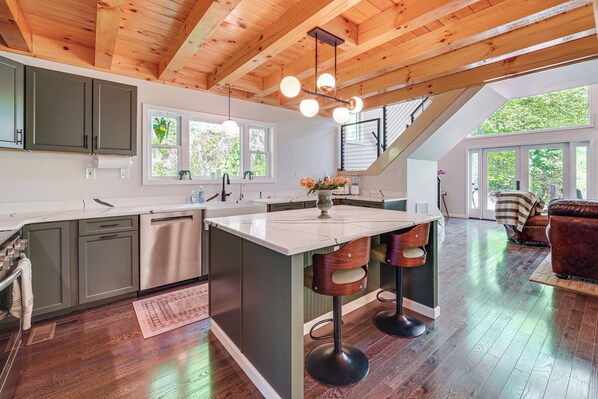A modern kitchen with a central island, bar stools, and a dining area with a sofa. - 'The Appalachian Hideaway' w/ Hiking Trails & Deck (Spencer)