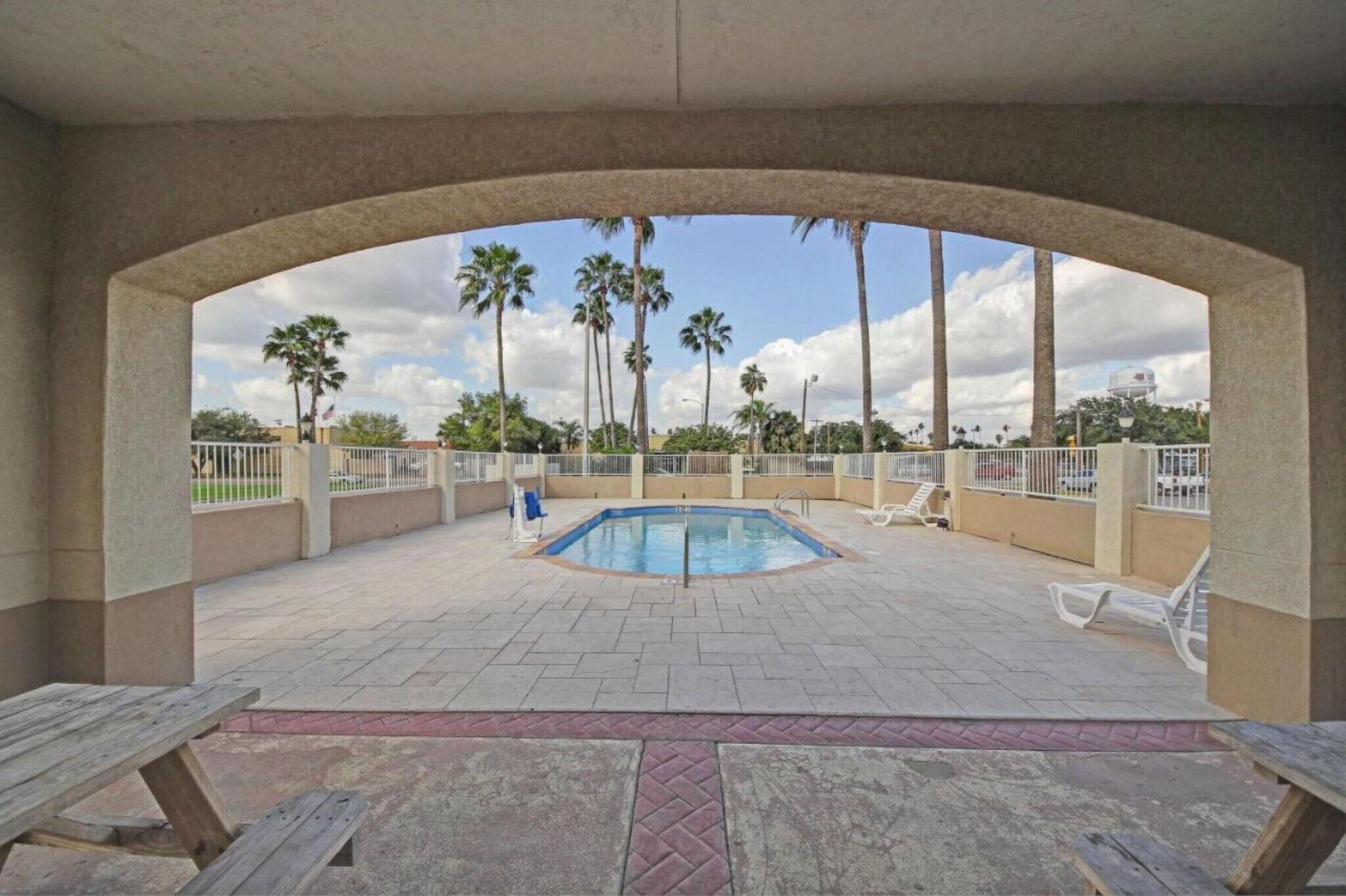 Zona de piscina al aire libre con vista a palmeras y un cielo despejado.