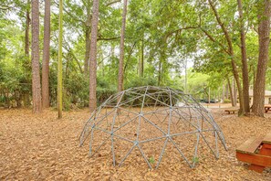 Une structure en forme de dôme géodésique métallique, située dans une zone boisée, avec des arbres et une table de pique-nique.