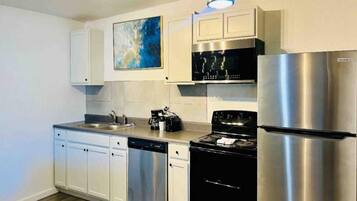 Una cocina moderna con electrodomésticos de acero inoxidable, armarios blancos y un cuadro abstracto azul en la pared.