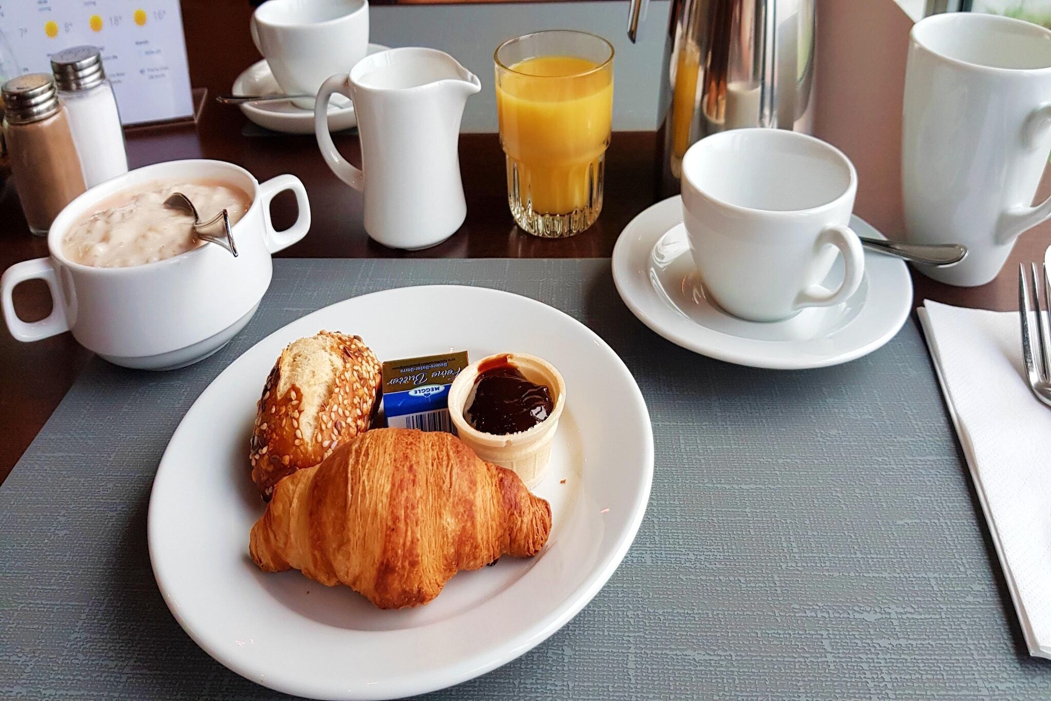 Un desayuno con croissants, mermelada y jugo de naranja sobre una mesa.