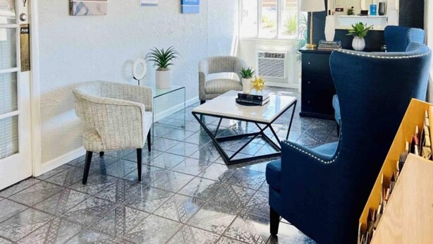 A hotel lobby with a reception desk, two armchairs, a coffee table, and a mirror.